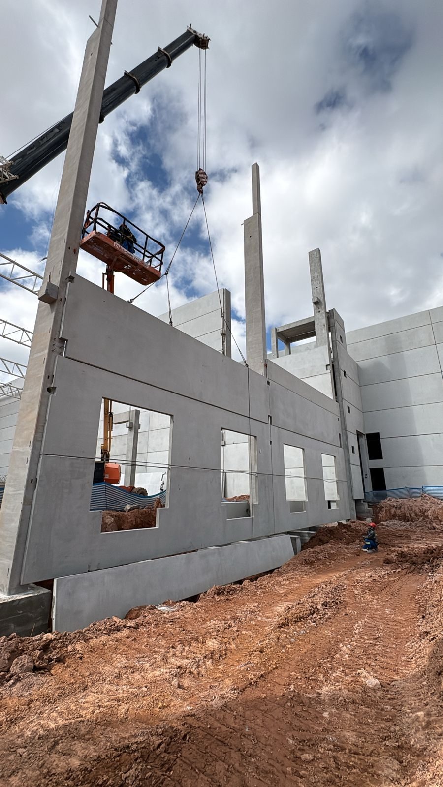Painel pré-moldado com as aberturas das janelas sendo posicionado, com plataforma elevatória ao lado