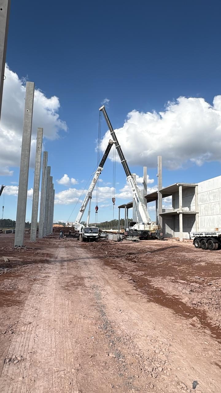 Dois guindastes montando os pilares pré-moldados, com a estrutura de pavimentos ao fundo