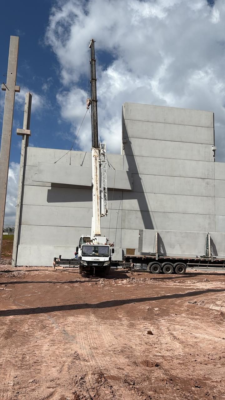 Guindaste diante da parede de painéis pré-moldados, com carreta trazendo mais painéis