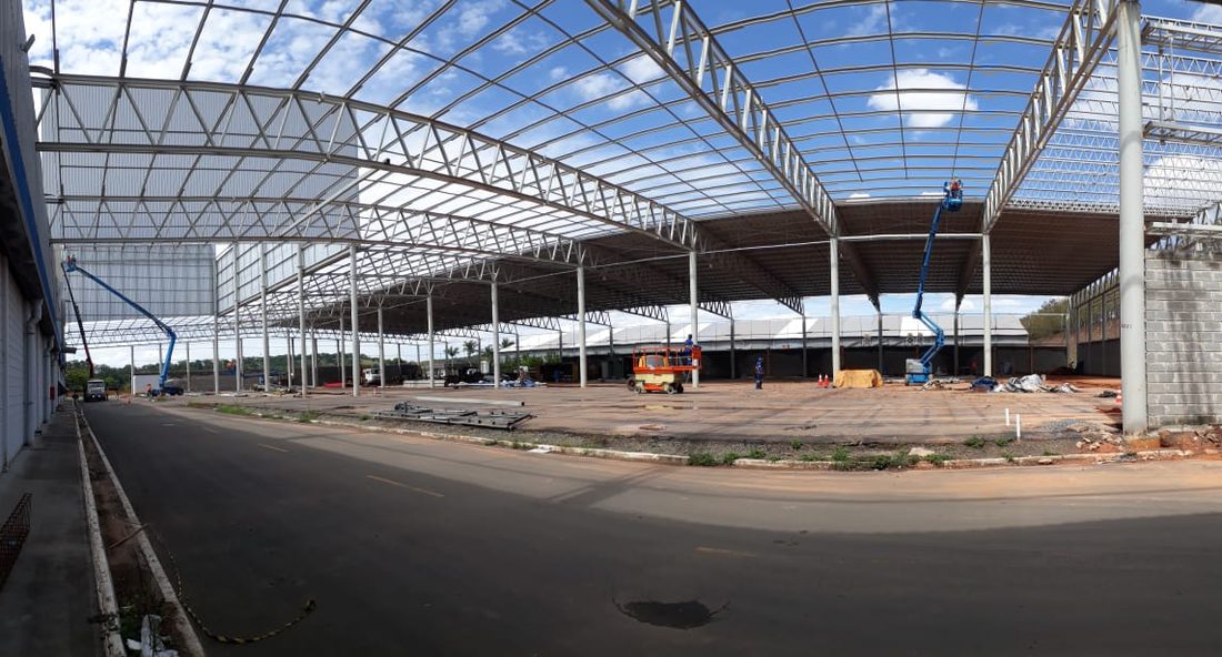 Cobertura metálica em montagem sobre o pátio, com plataformas elevatórias trabalhando nas treliças
