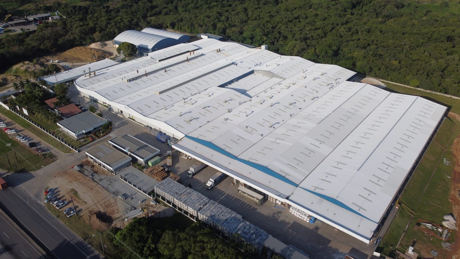 Vista aérea da planta da Deca Louças em Recife, com cobertura metálica de grande extensão cercada por mata