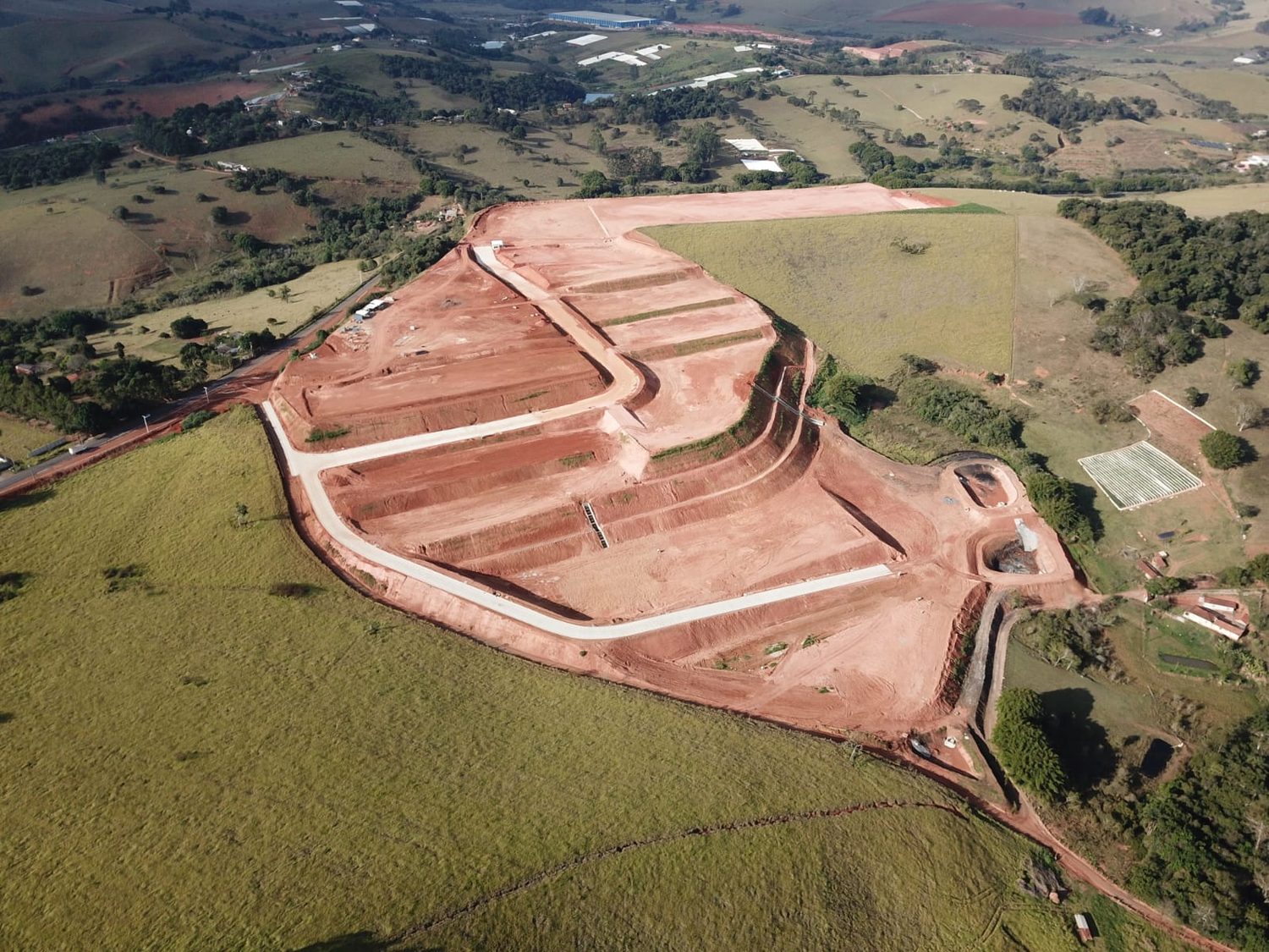 Vista aérea do platô de terraplanagem do condomínio industrial em Estiva, com taludes em bancada no meio do pasto
