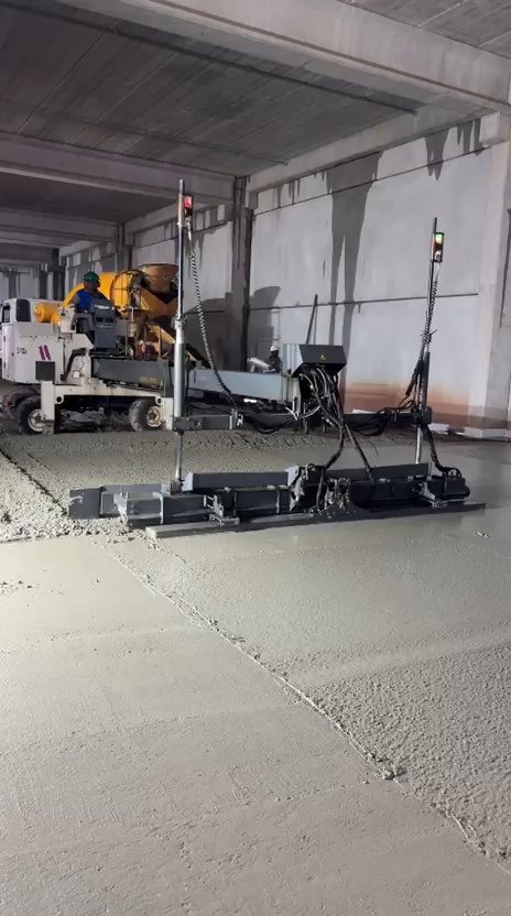 Régua laser nivelando o concreto com a equipe espalhando à frente