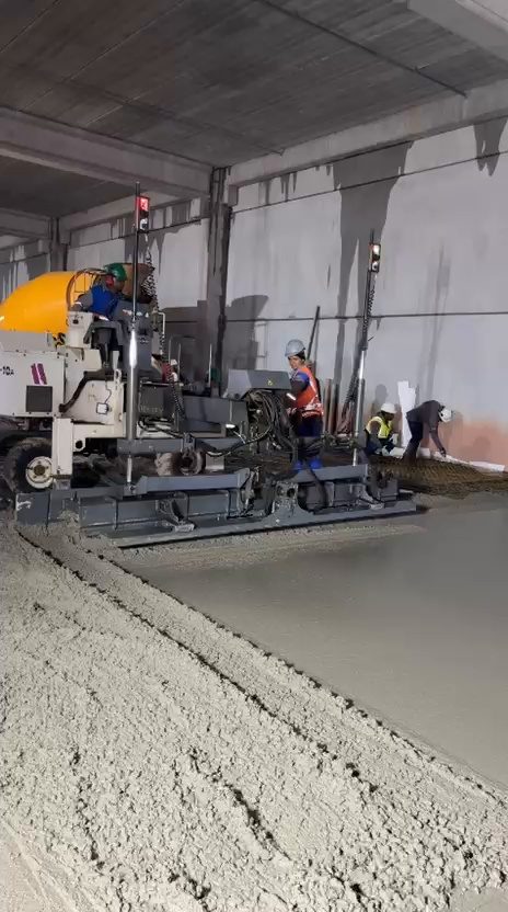 Régua laser e caminhão betoneira lançando concreto junto à parede do galpão